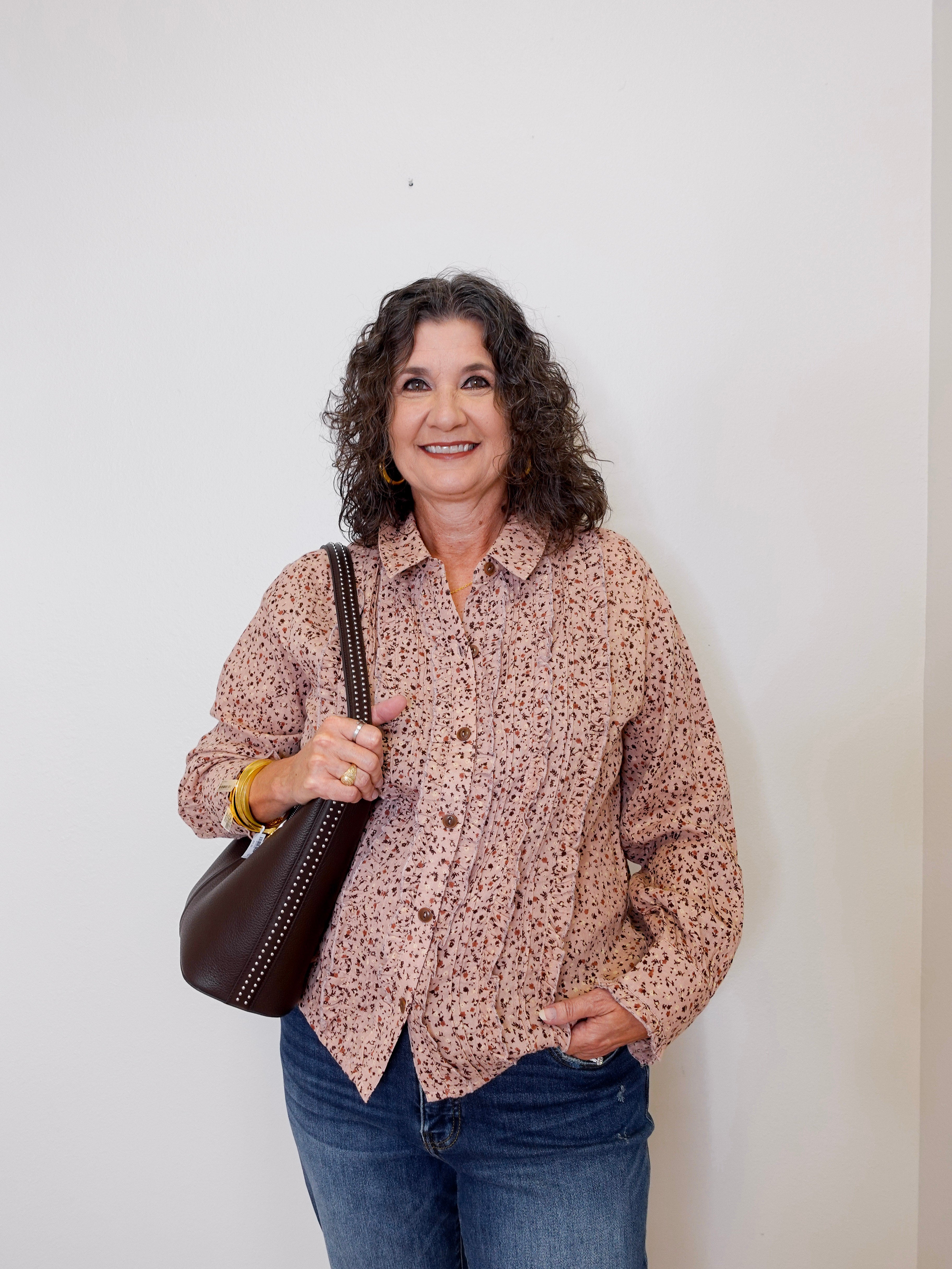Woman wearing a patterned shirt and jeans, holding a brown bag against a white background