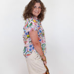 Woman wearing a colorful floral shirt and beige shorts against a white background