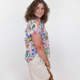 Woman wearing a colorful floral shirt and beige shorts against a white background