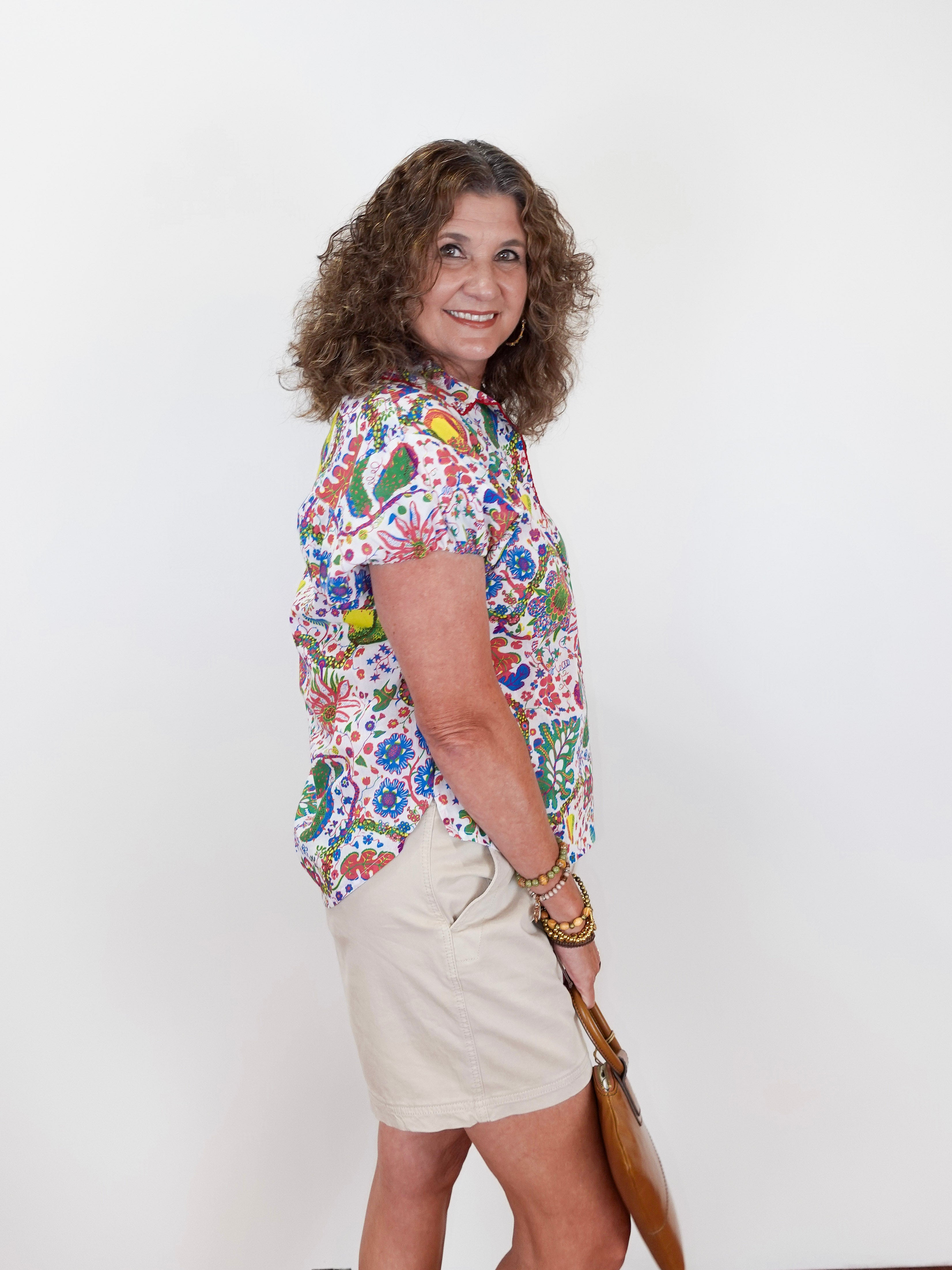 Woman wearing a colorful floral shirt and beige shorts against a white background
