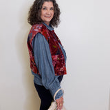 Woman wearing a floral vest over a denim shirt with a white background