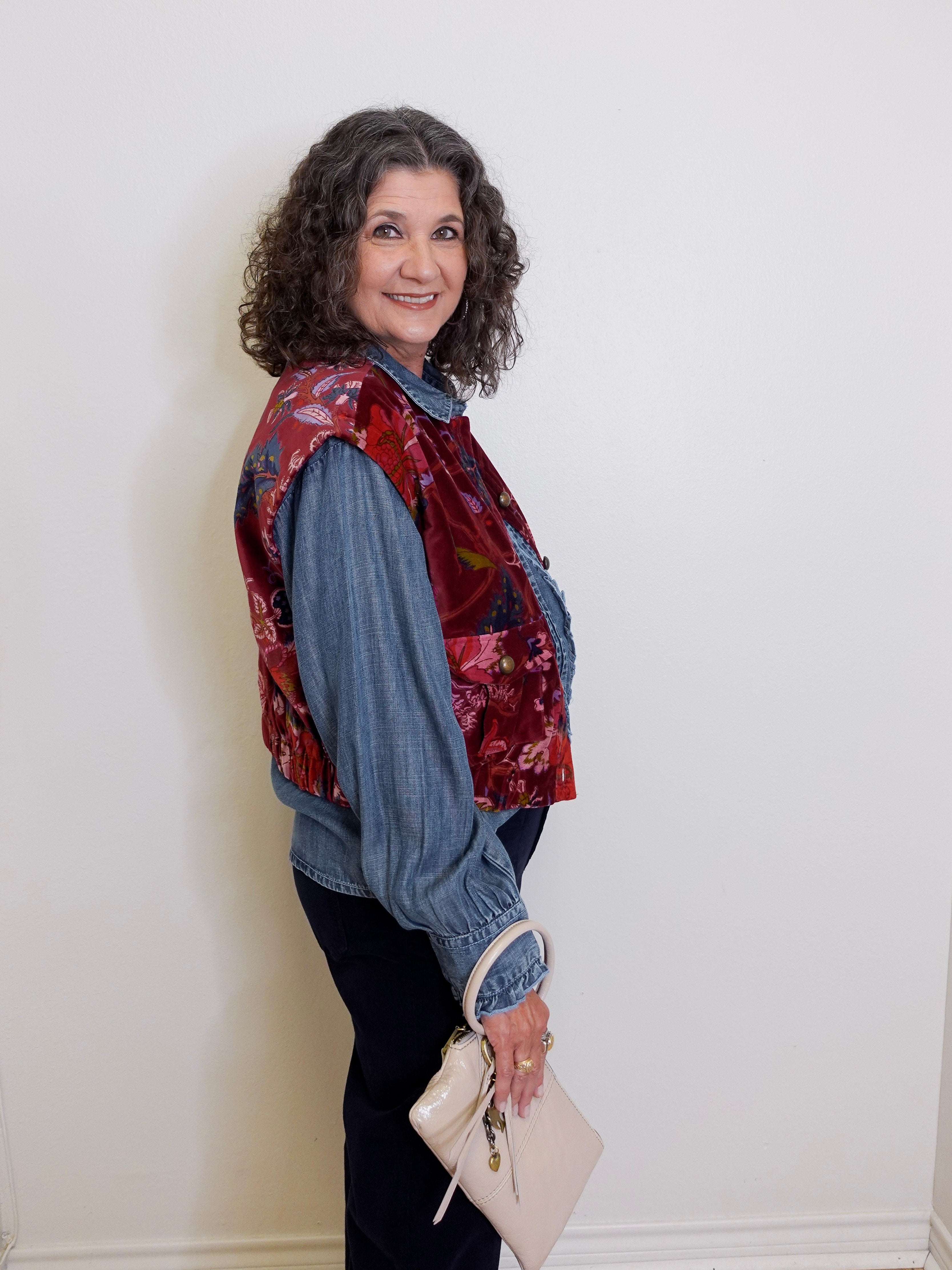Woman wearing a floral vest over a denim shirt with a white background