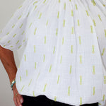White blouse with yellow text pattern worn by a person against a neutral background