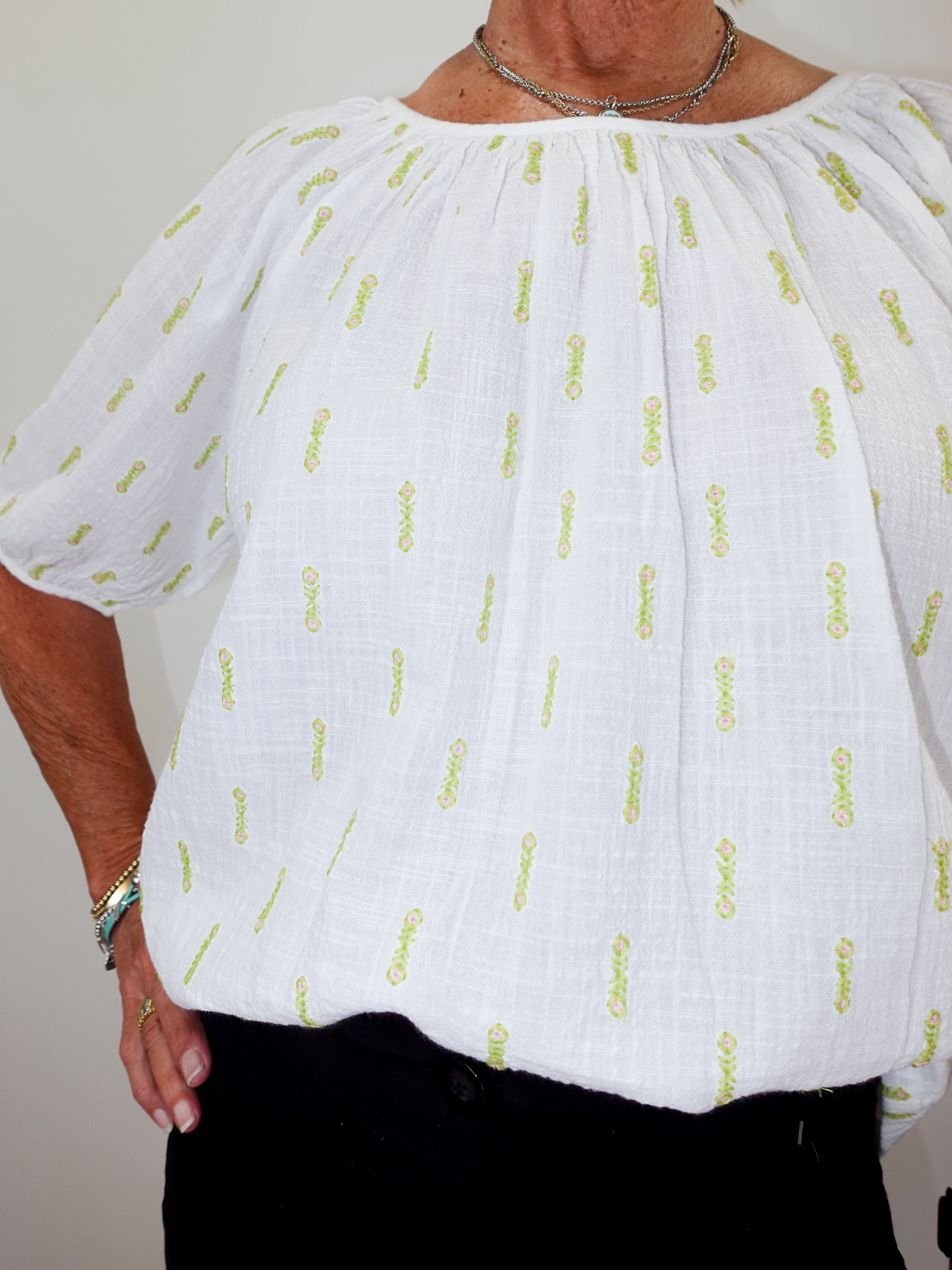 White blouse with yellow text pattern worn by a person against a neutral background