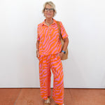 Person wearing a bright orange and pink patterned outfit against a white wall.