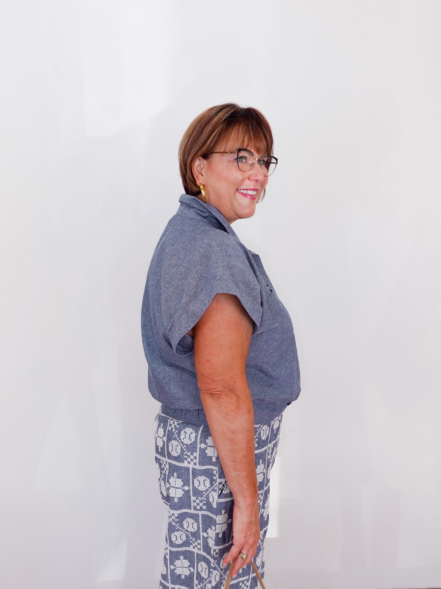 Woman wearing a blue shirt and patterned pants against a white background