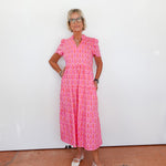 Woman wearing a pink patterned dress standing against a white wall.
