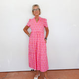 Woman wearing a pink patterned dress standing against a white wall.