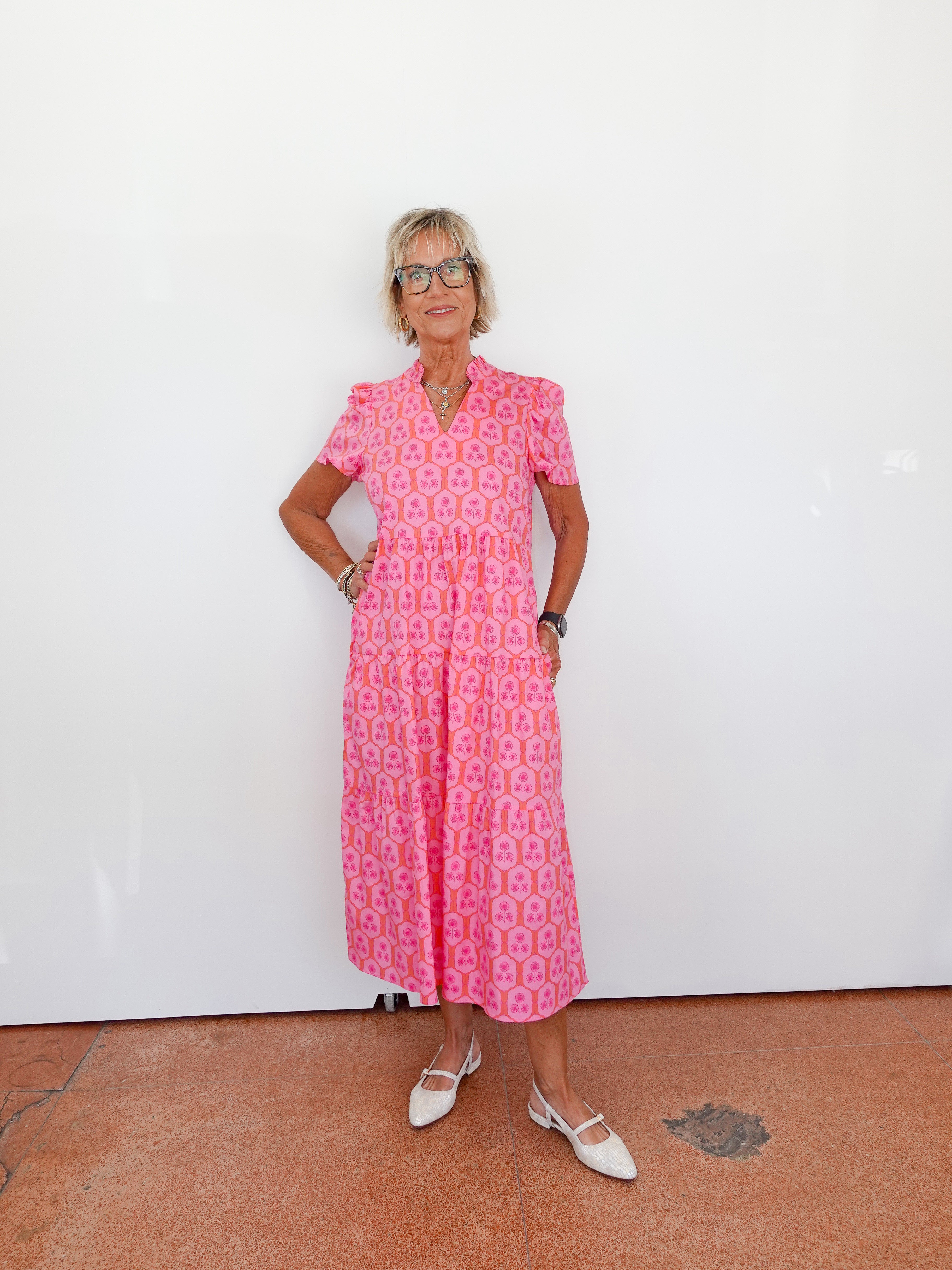 Woman wearing a pink patterned dress standing against a white wall.