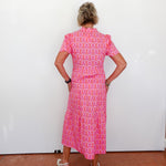 Person wearing a pink patterned dress standing against a white wall.