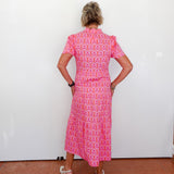 Person wearing a pink patterned dress standing against a white wall.