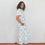 Woman wearing a white dress with green patterns against a plain background