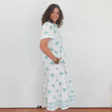 Woman wearing a white dress with green patterns against a plain background