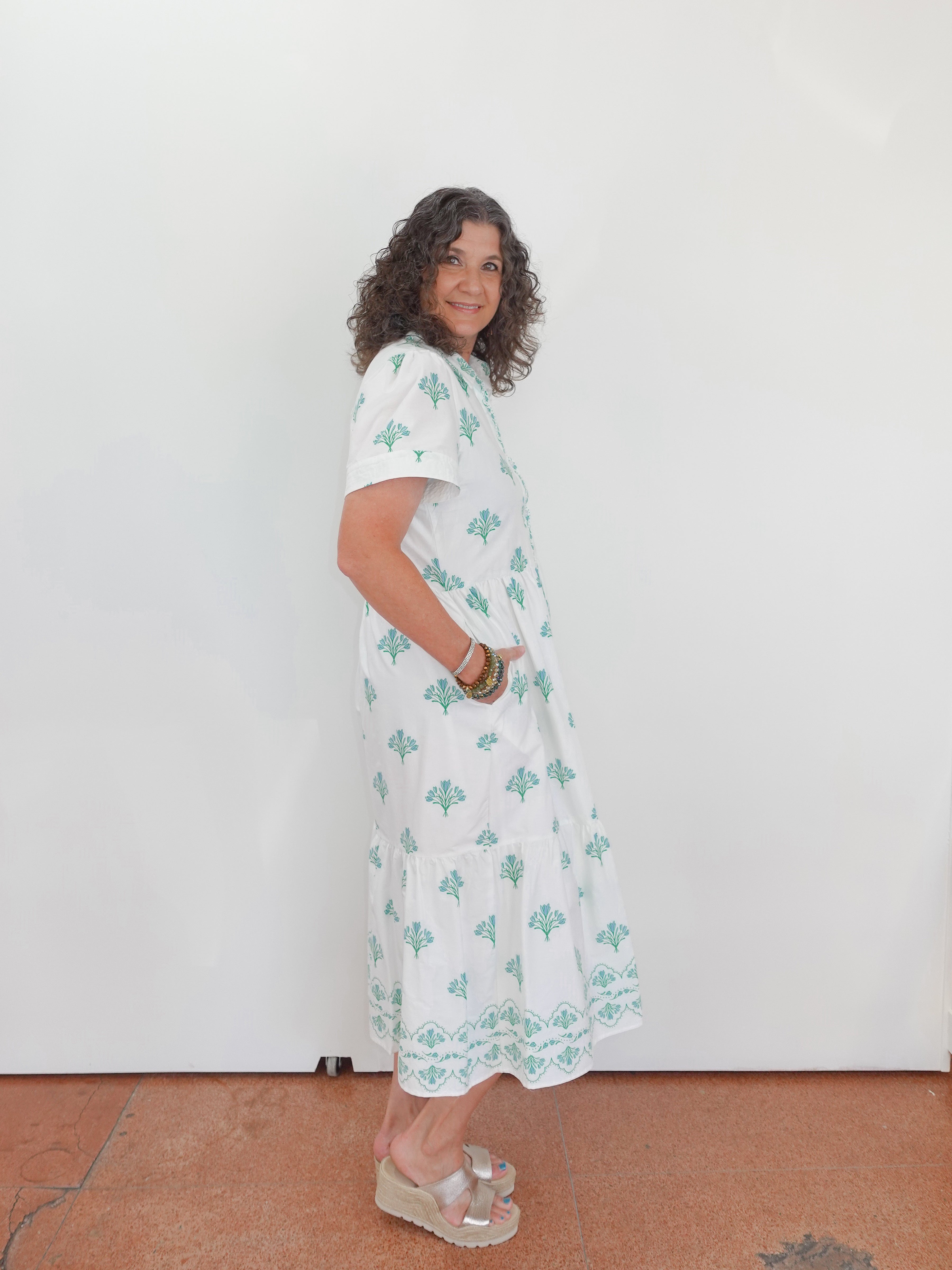 Woman wearing a white dress with green patterns against a plain background