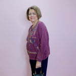 Woman wearing a purple sweater with floral patterns against a light pink wall.