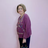 Woman wearing a purple sweater with floral patterns against a light pink wall.
