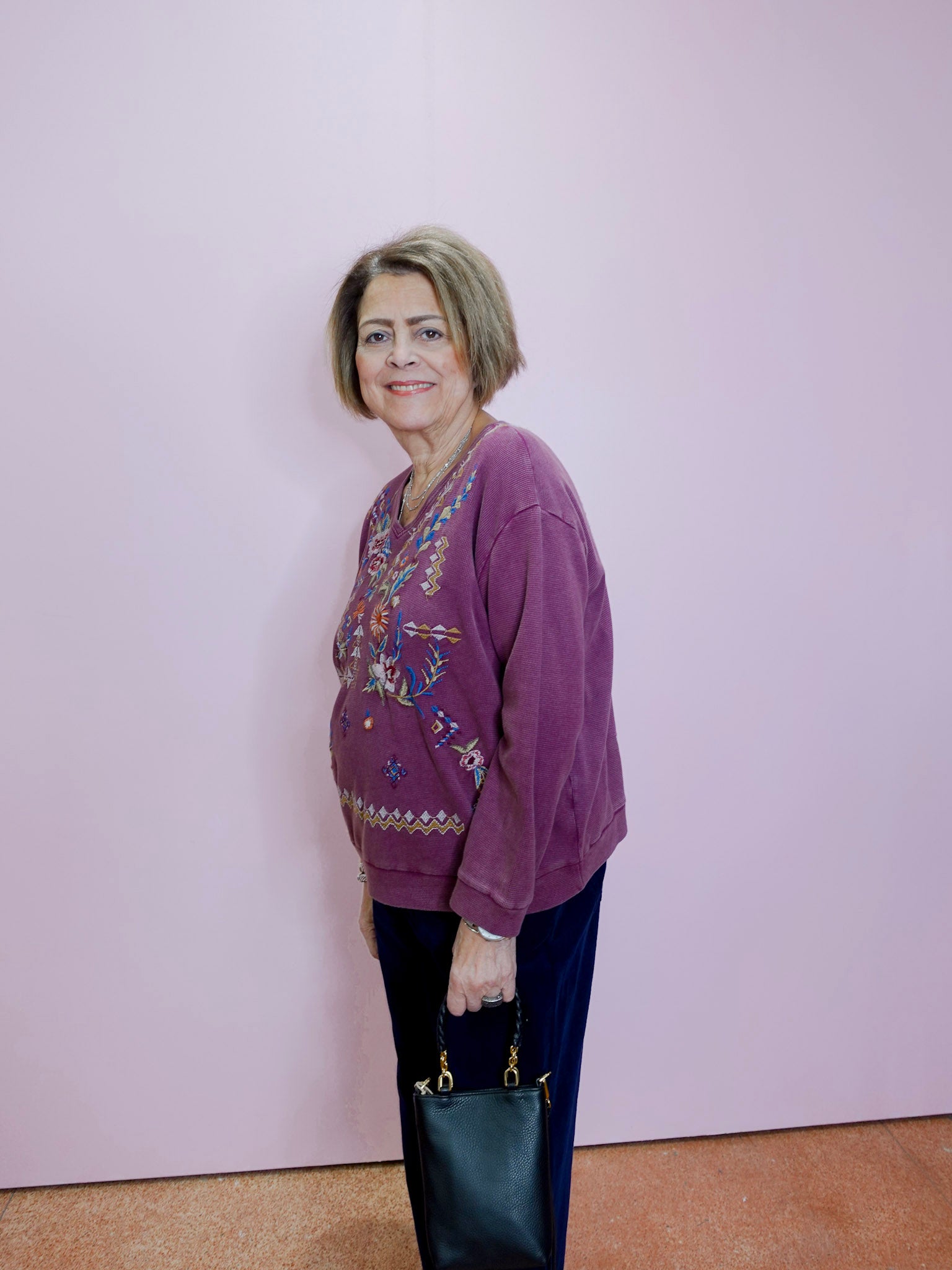 Woman wearing a purple sweater with floral patterns against a light pink wall.