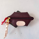 Brown leather pouch with gold zipper and red ribbon on a white background