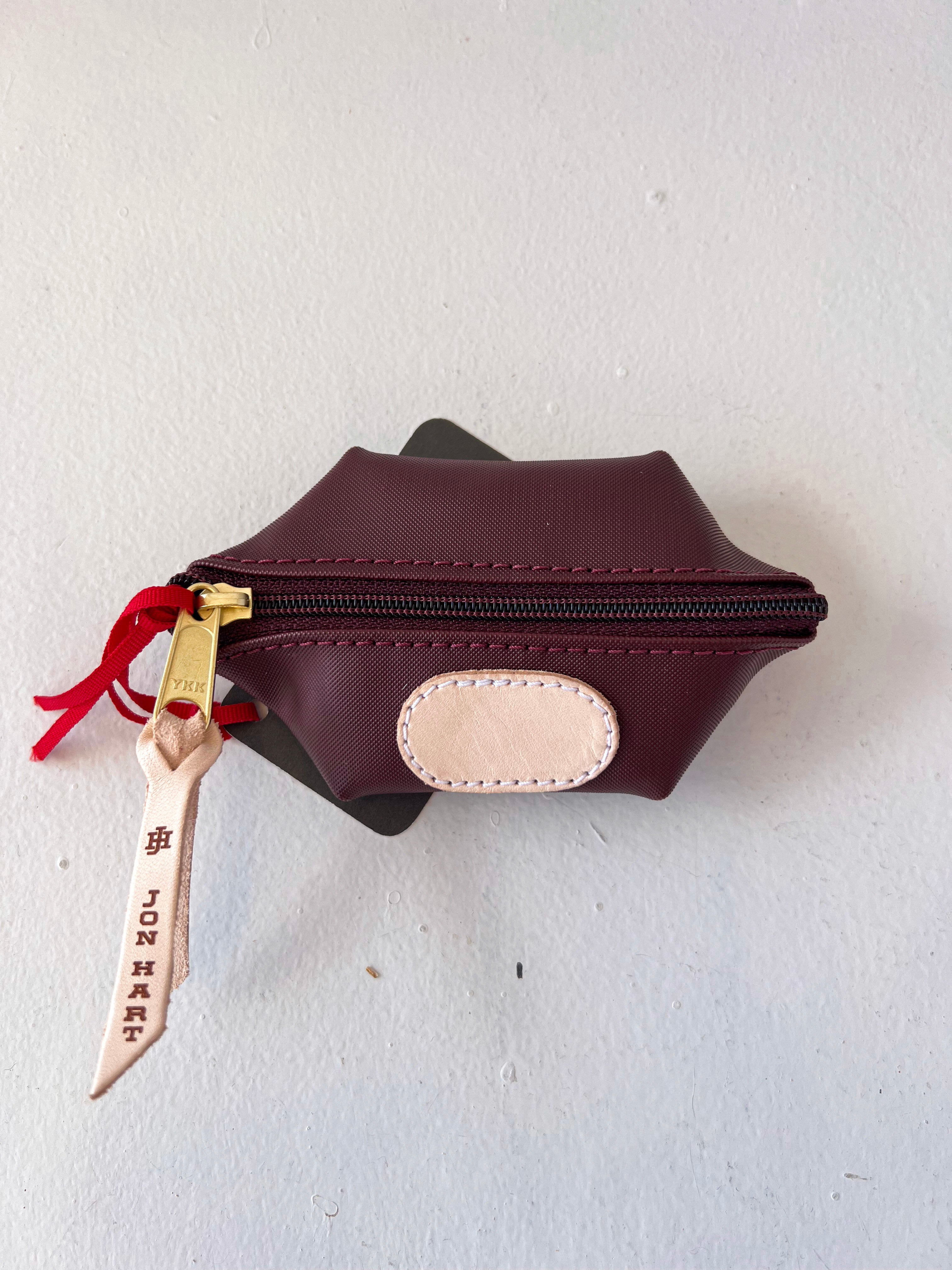 Brown leather pouch with gold zipper and red ribbon on a white background