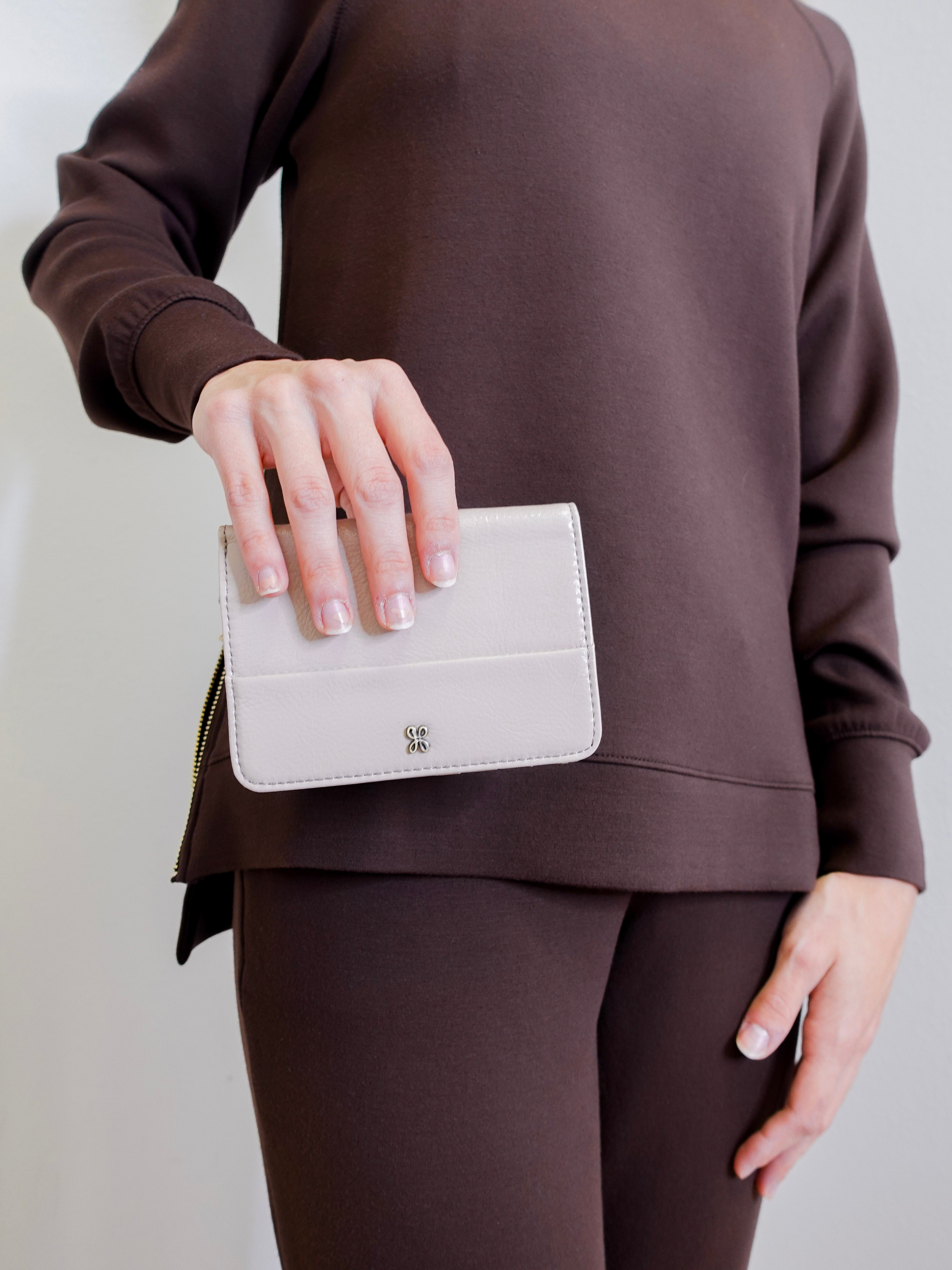 woman holding Front view of the HOBO Jill Bi-Fold Wallet in stone gloss aniline leather.