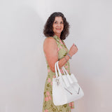 Woman in a green checkered dress holding a white handbag against a plain background