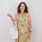 Woman wearing a green checkered dress with floral patterns, holding a white handbag against a plain background.