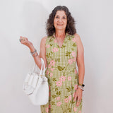 Woman wearing a green checkered dress with floral patterns, holding a white handbag against a plain background.