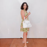 Woman in a green checkered dress holding a white handbag against a white wall.