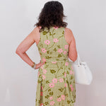 Person wearing a green checkered dress with pink floral patterns, standing against a white wall.