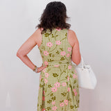 Person wearing a green checkered dress with pink floral patterns, standing against a white wall.