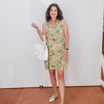 Woman in a green checkered dress holding a white bag against a white wall.
