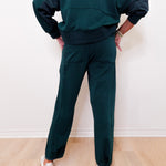 Person wearing a dark green tracksuit against a white wall.