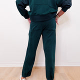Person wearing a dark green tracksuit against a white wall.