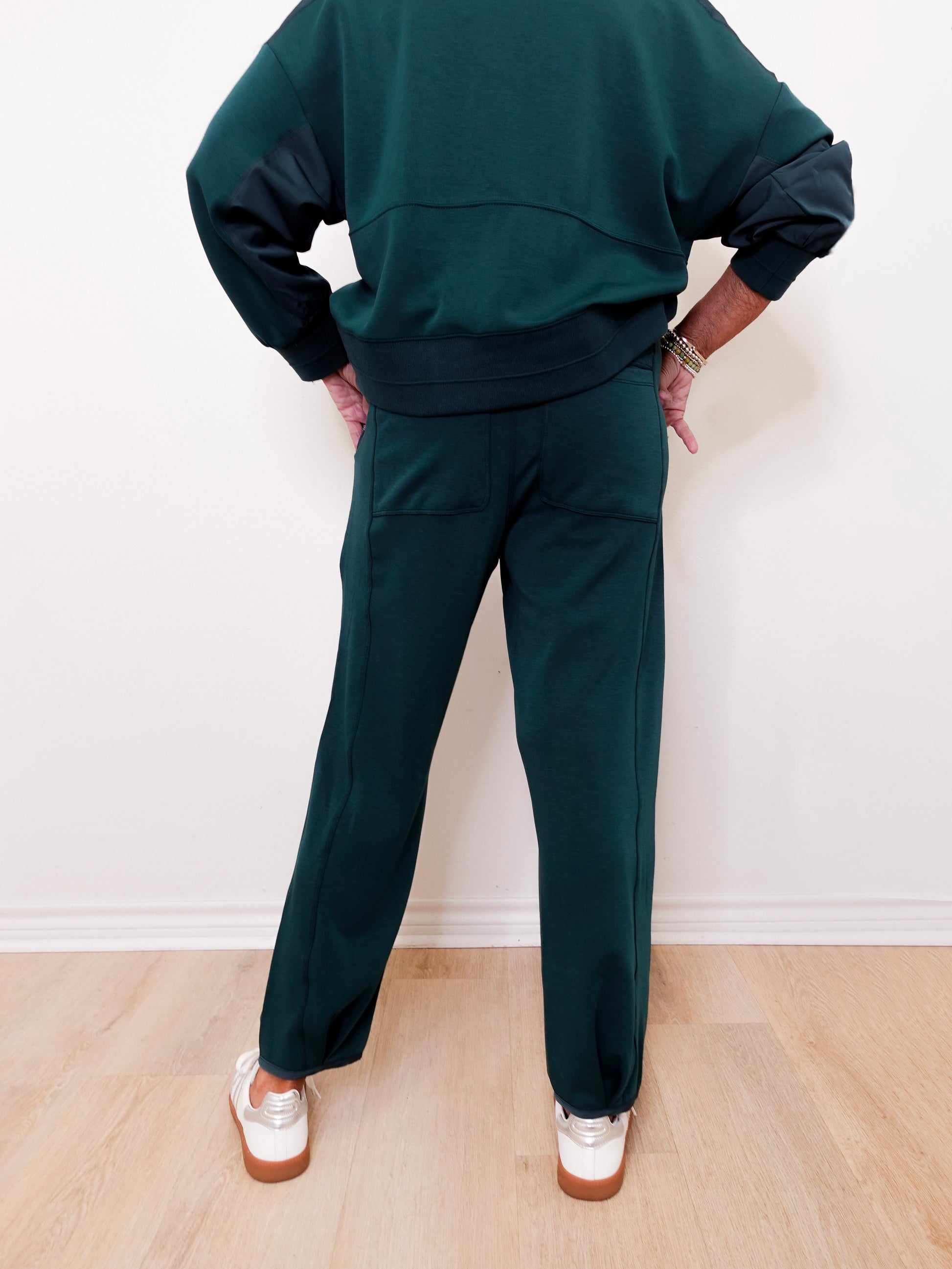Person wearing a dark green tracksuit against a white wall.