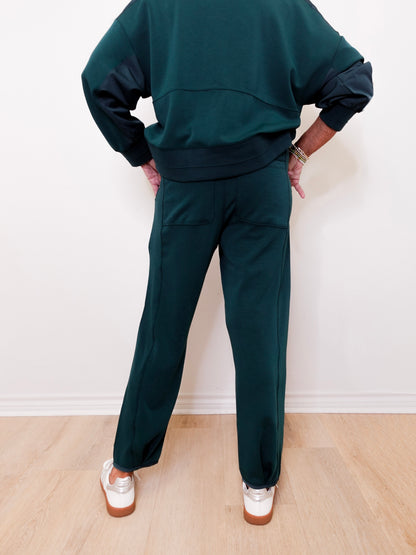 Person wearing a dark green tracksuit against a white wall.