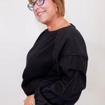 Woman wearing a black top and glasses against a plain background