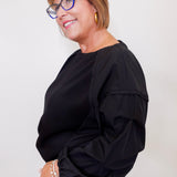 Woman wearing a black top and glasses against a plain background