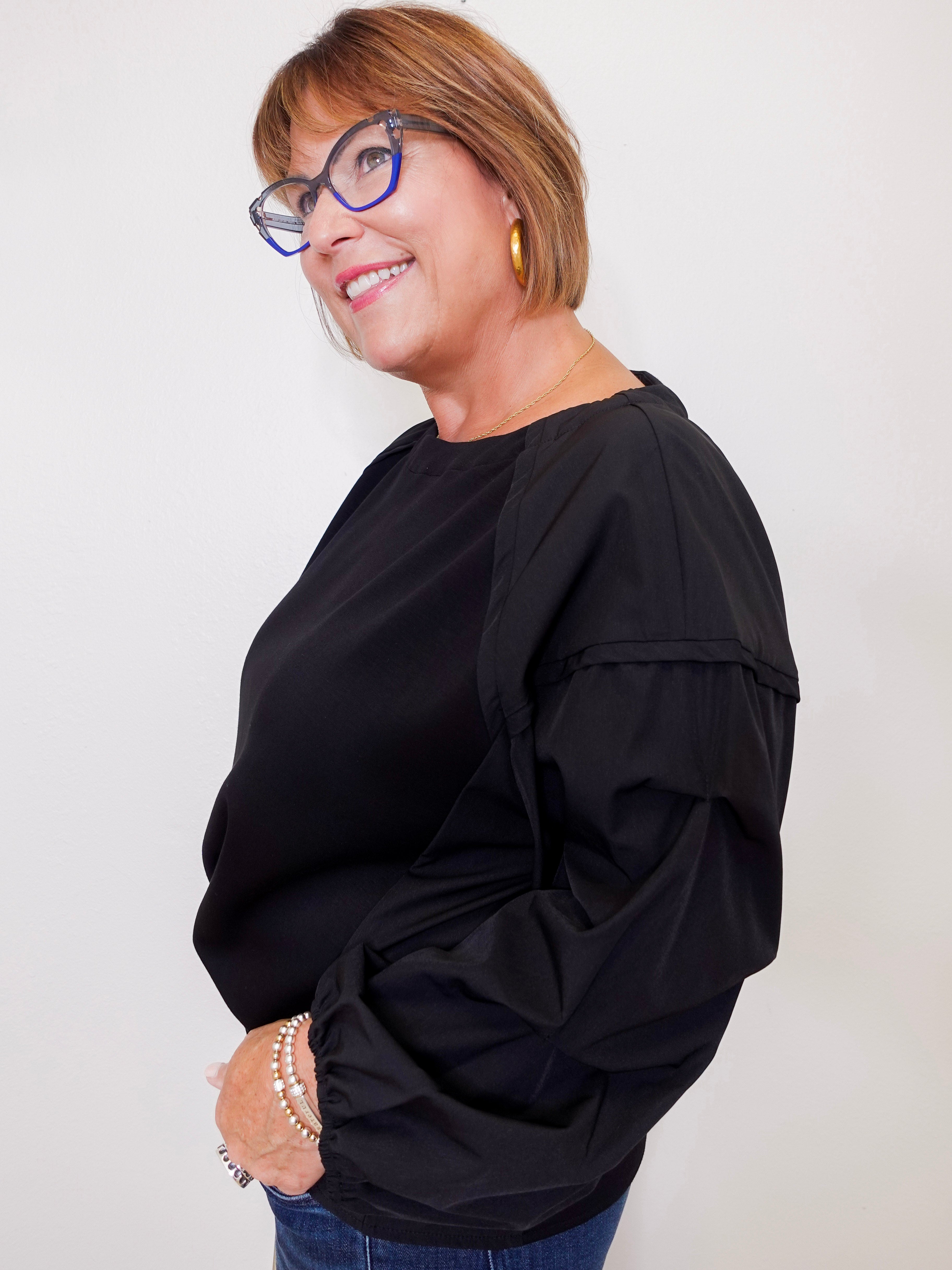 Woman wearing a black top and glasses against a plain background