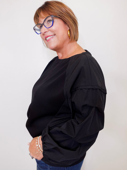 Woman wearing a black top and glasses against a plain background