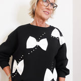 Person wearing a black sweater with white bow designs on a plain background