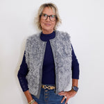 Person wearing a gray vest over a blue shirt with a white background