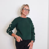 Woman wearing a green sweater with pearl embellishments against a white background