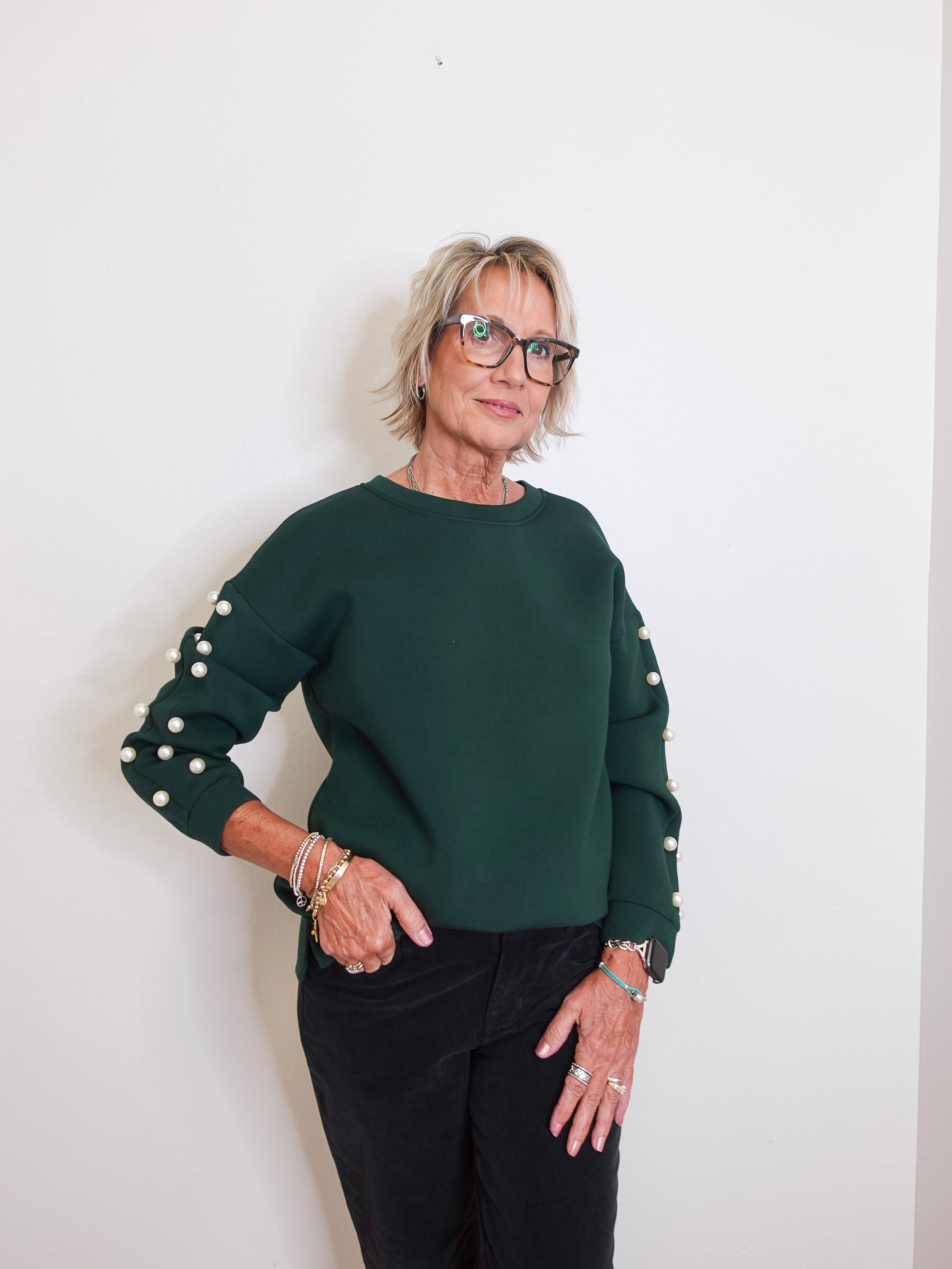 Woman wearing a green sweater with pearl embellishments against a white background