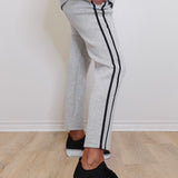 Person wearing gray sweatpants with black stripes and black sneakers on a light wooden floor.