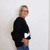 Person wearing a black sweater with a white design and blue jeans against a plain background