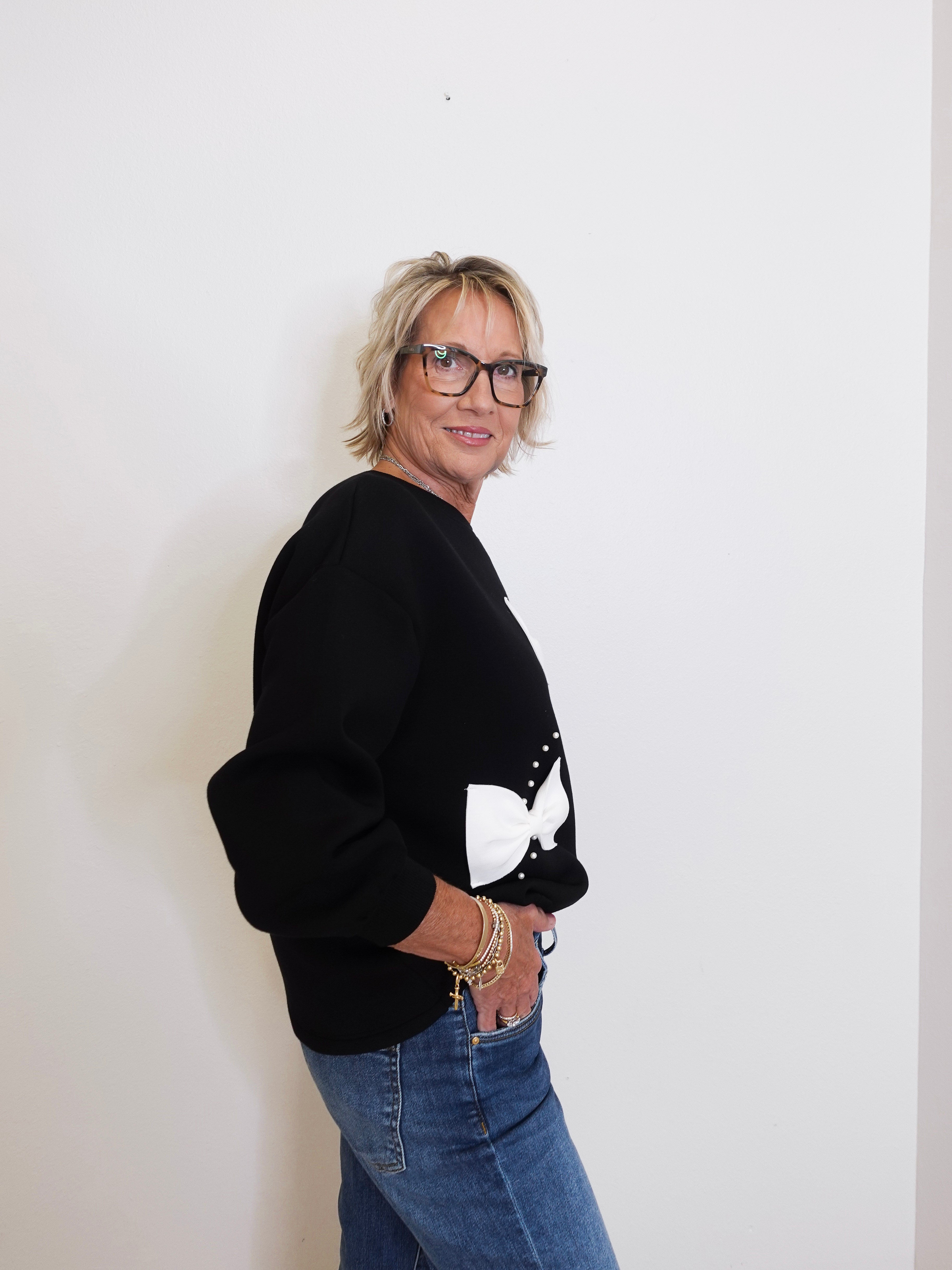 Person wearing a black sweater with a white design and blue jeans against a plain background