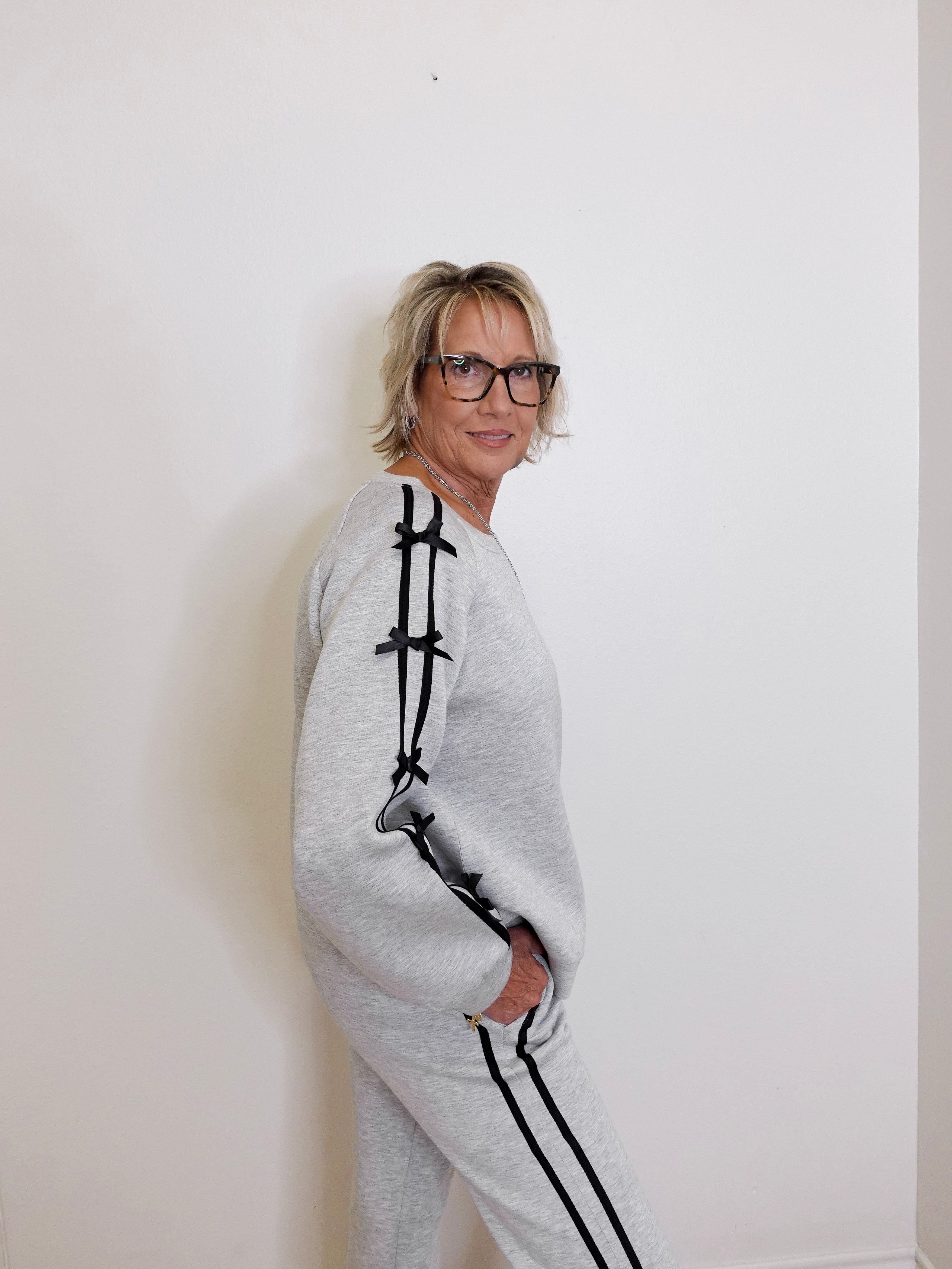 Person wearing a gray tracksuit with black accents against a white wall