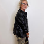 Person wearing a black jacket and camouflage pants against a white wall