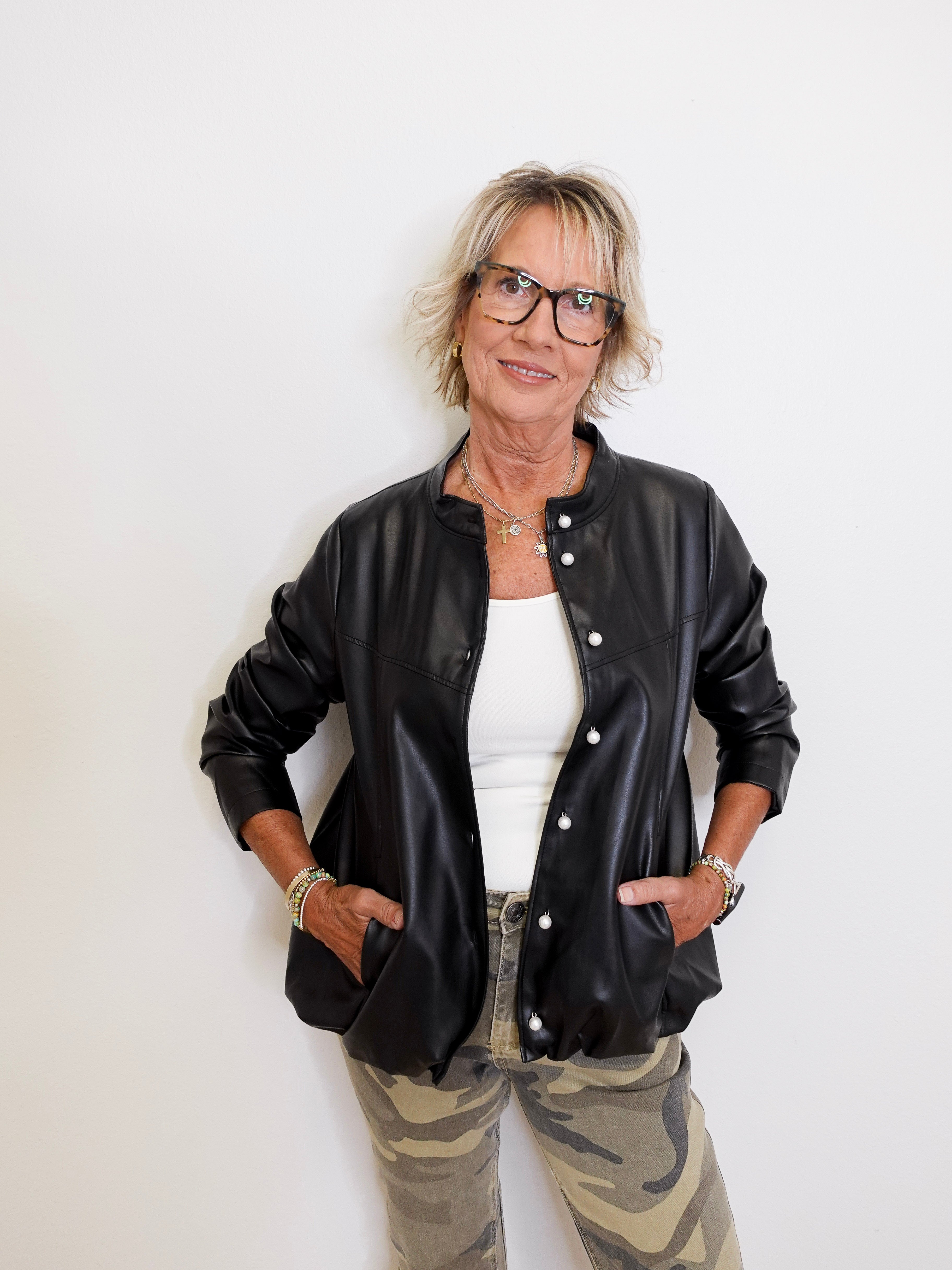Person wearing a black leather bomber jacket, white shirt, and camouflage pants against a white background