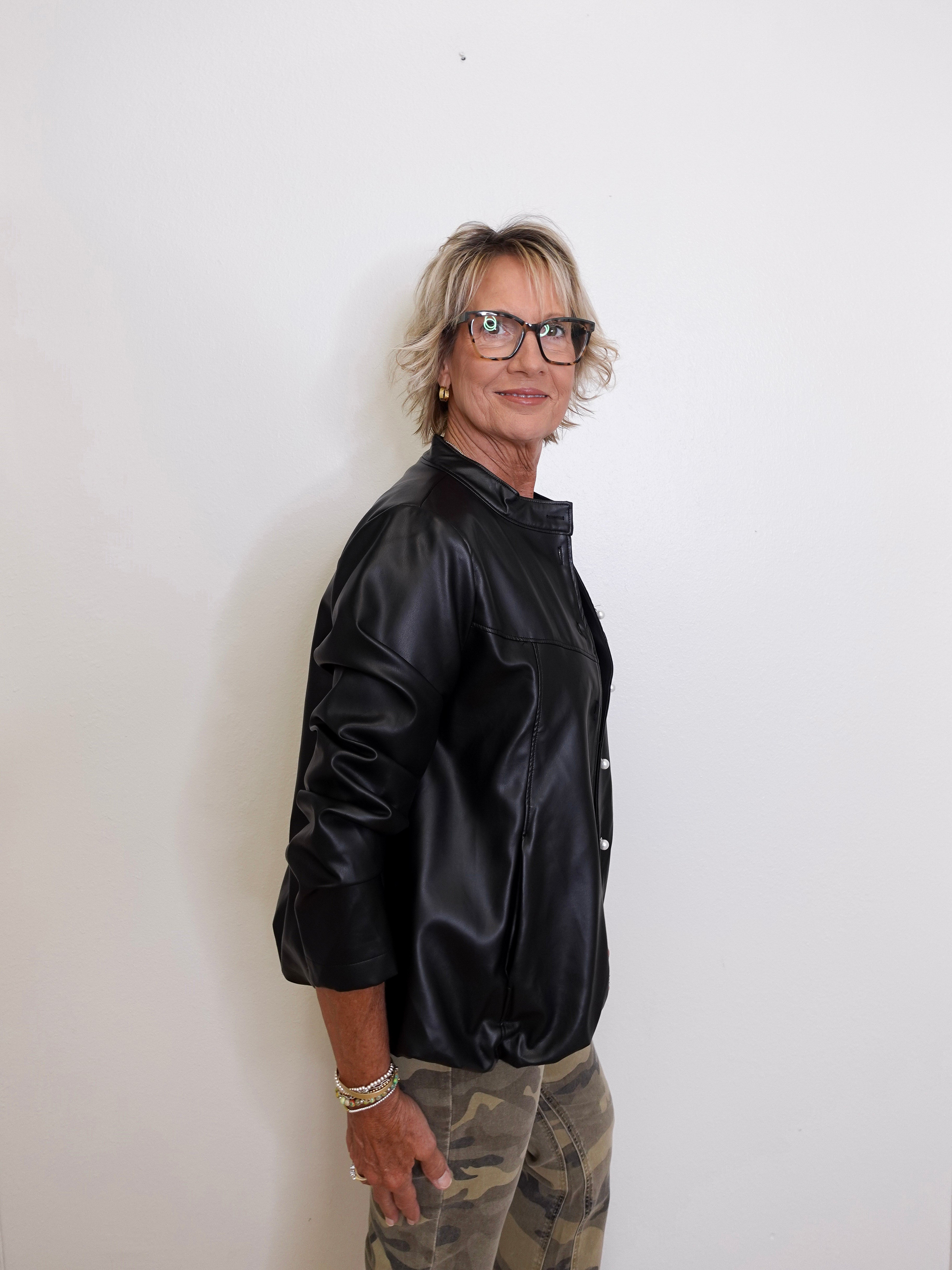 Person wearing a black jacket and camouflage pants against a white background